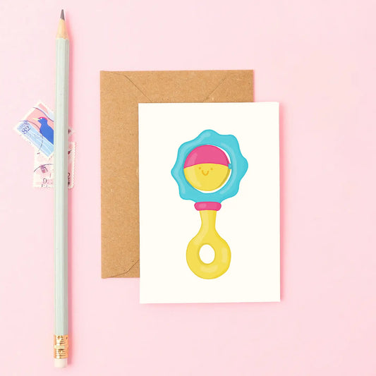 Mini new baby card with smiling blue, pink and yellow hand drawn rattle