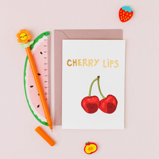 Cherry Lips greeting card featuring two smiling cherries with gold foil lettering on a contemporary cream background.