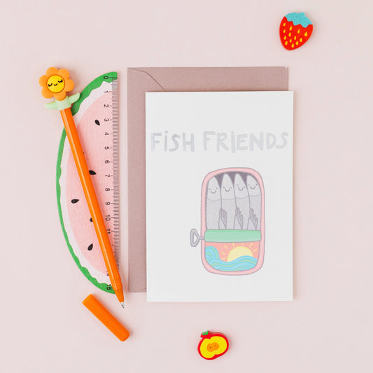 Fish Friends greeting card featuring smiling sardines in a tin with silver foil lettering on a contemporary white background.
