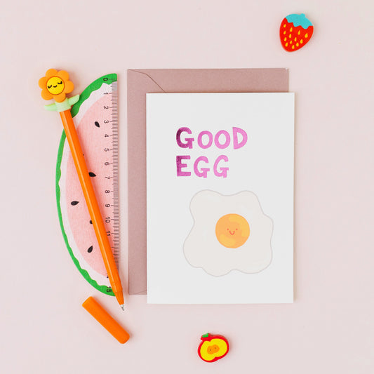 Good Egg greeting card featuring a smiling fried egg with pink foil lettering on a contemporary white background.