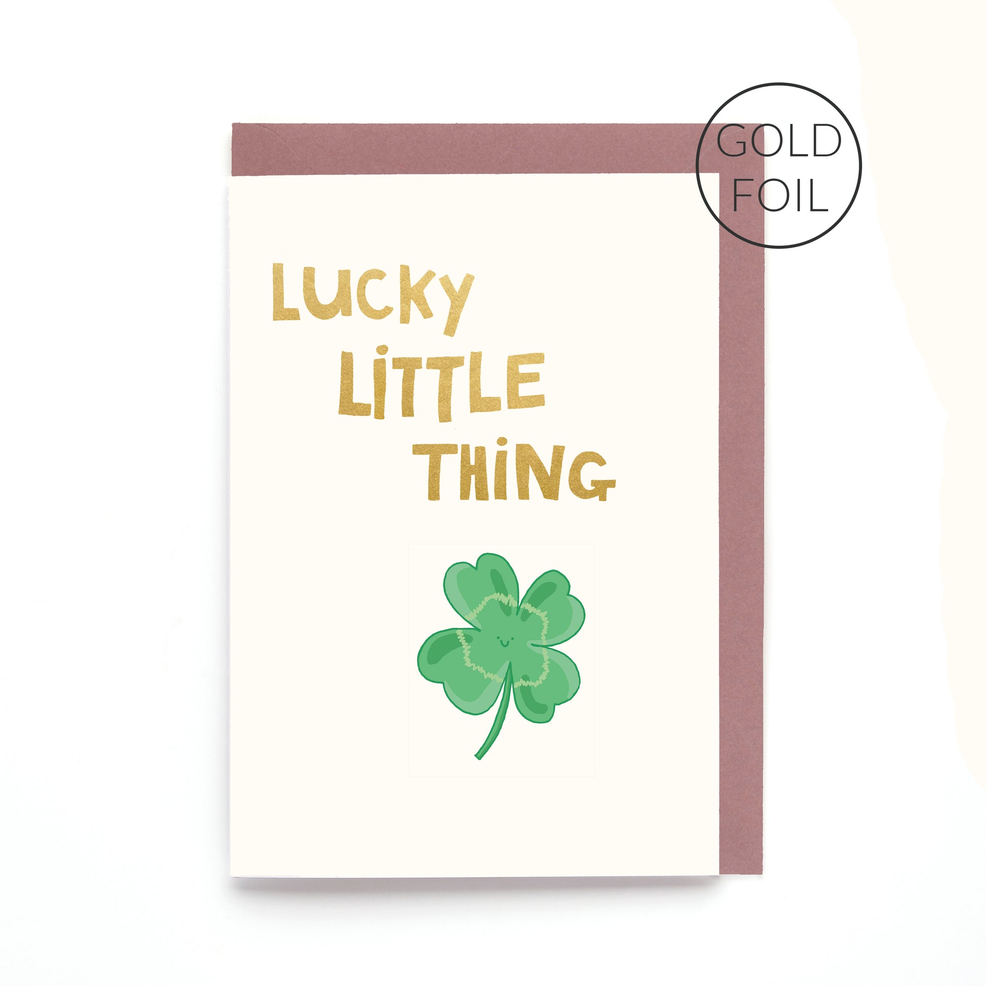 Lucky Little Thing greeting card featuring a smiling four leaf clover with gold foil lettering on a contemporary white background.