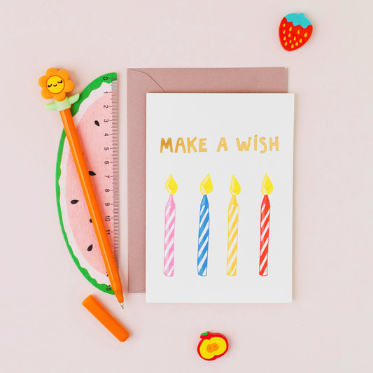 Make A Wish birthday card featuring four smiling birthday candles with gold foil lettering on a contemporary white background.