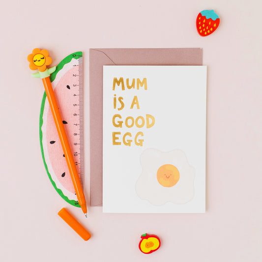 Mum Is A Good Egg greeting card featuring a smiling fried egg with gold foil lettering on a contemporary white background.
