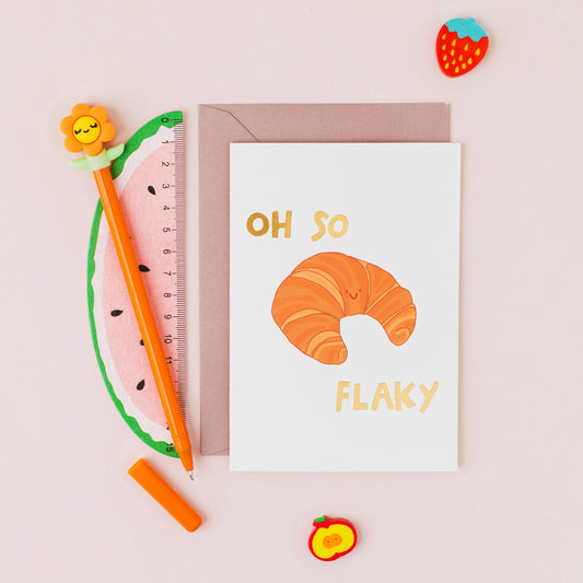 Oh So Flaky greeting card featuring a smiling croissant with gold foil lettering on a contemporary white background.