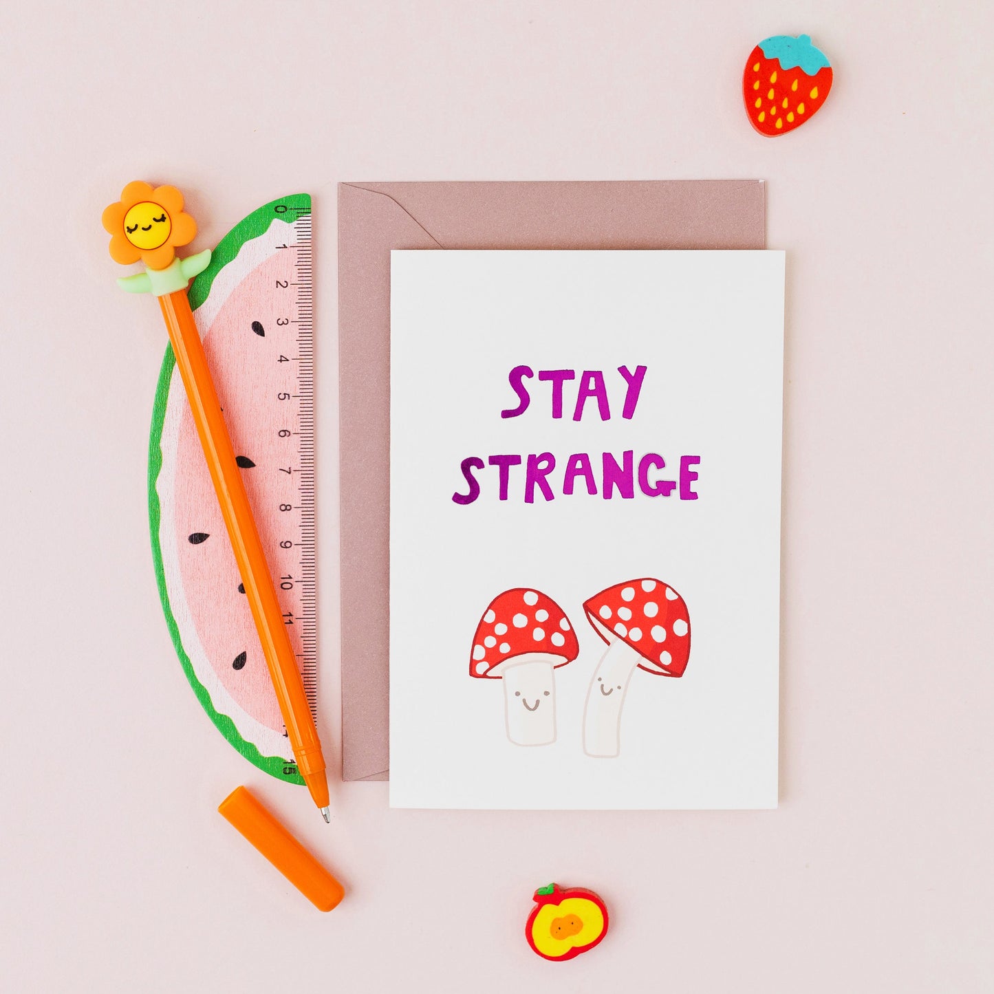 Hand drawn fly agaric mushroom greeting card reading "Stay Strange" with gold foil lettering on a white background.
