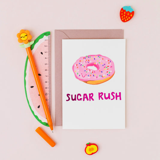 Hand drawn pink doughnut greeting card reading "Sugar Rush" finished with gold foil on a white background.