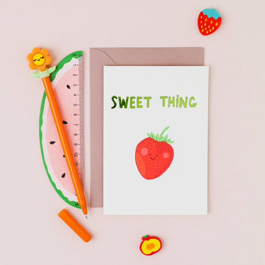 Hand drawn smiling strawberry greeting card with the words 'Sweet Thing' in green hot foil on a white background.