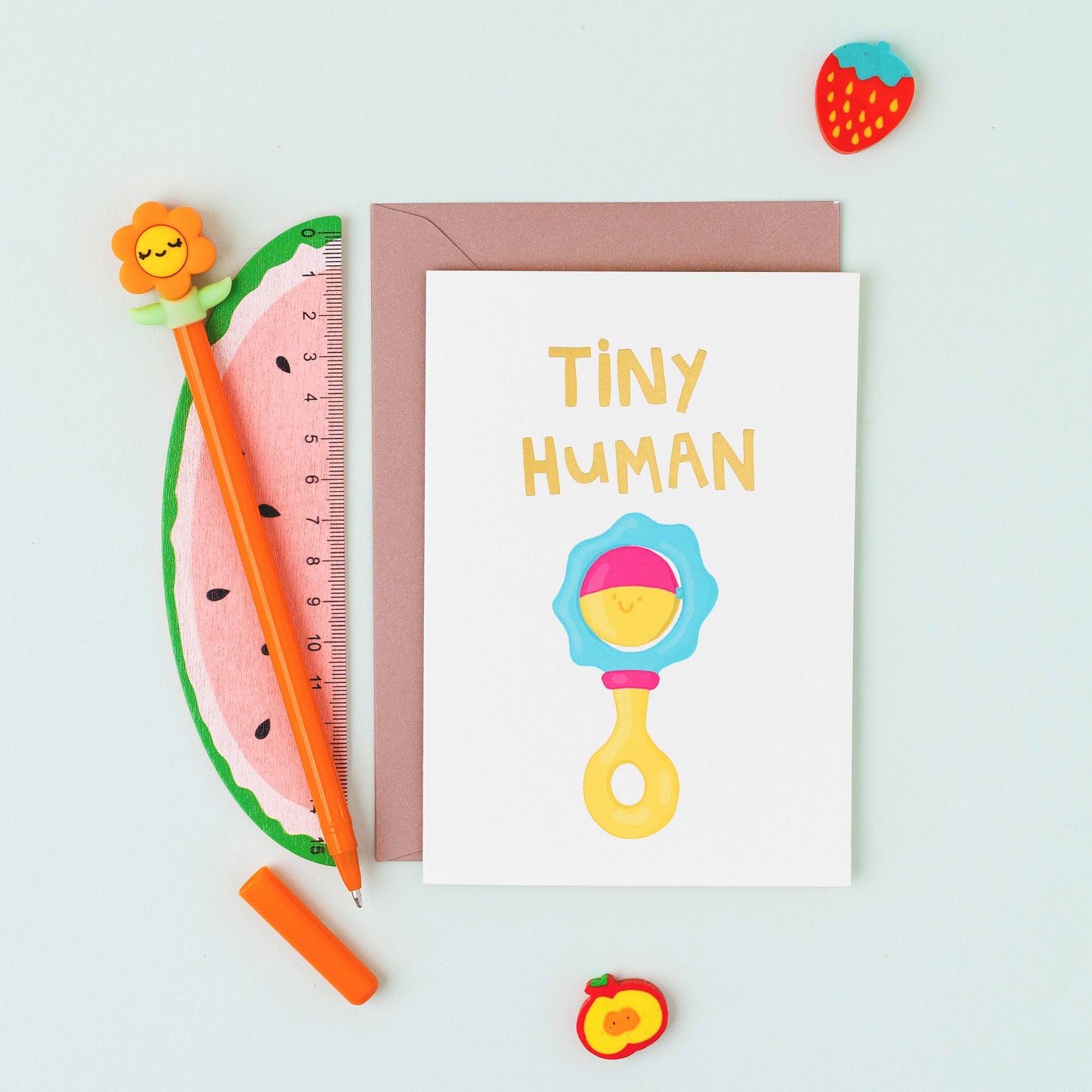 Hand drawn smiling baby rattle greeting card with the words 'Tiny Human' in gold foil on a white background.